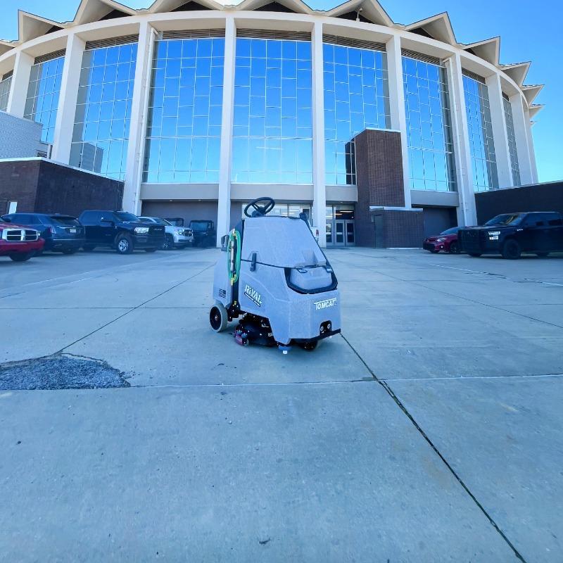 Tomcat Stand On Floor Scrubbers Rival event venues concrete A Tomcat Rival stand on battery floor scrubber is cleaning the concrete sidewalks af a concert and entertainment venue.